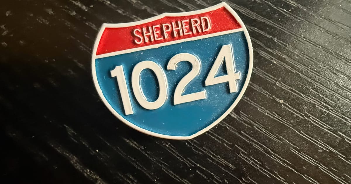 A pin shaped and colored like a U.S. Interstate Highway sign, reading "Shepherd" in the upper red portion and with the number "1024" in the lower blue portion.