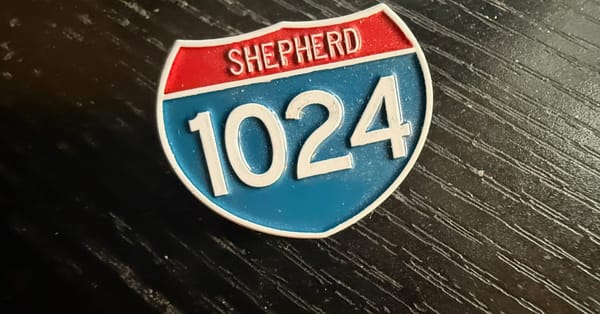 A pin shaped and colored like a U.S. Interstate Highway sign, reading "Shepherd" in the upper red portion and with the number "1024" in the lower blue portion.